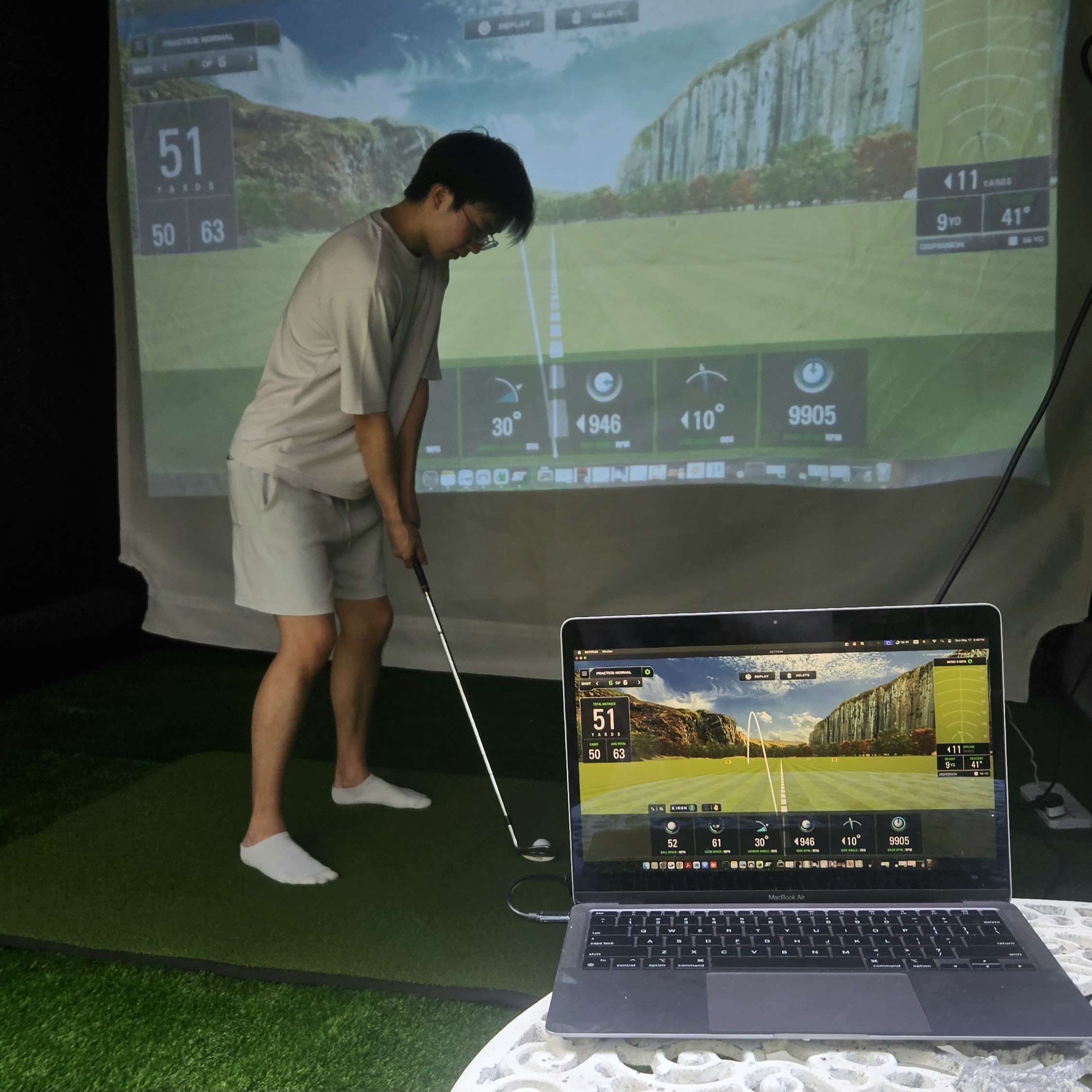 Player mid-swing on the Golf Anywhere simulator with laptop showing live data